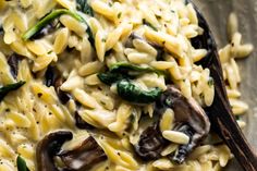 pasta with mushrooms, spinach and cheese on a wooden spoon in a glass bowl