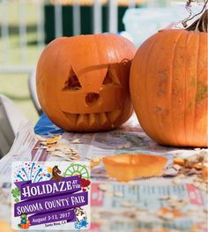 two carved pumpkins sitting on top of a table next to a sign that says holiday at sonoma county fair