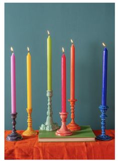 seven candles are lined up next to each other on an orange table cloth with a blue wall in the background