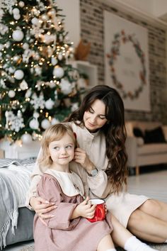 a mother and daughter sitting in front of a christmas tree