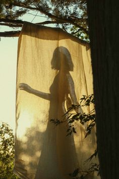 a woman standing next to a tree with a curtain hanging from it's side