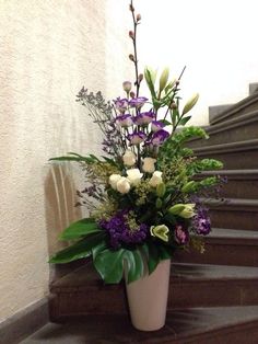 a white vase filled with purple and white flowers on top of a wooden floor next to stairs