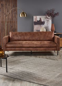 a brown leather couch sitting on top of a wooden floor next to a table and lamp