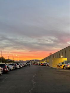 a parking lot filled with lots of parked cars under a cloudy sky at sunset or dawn