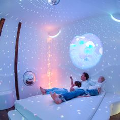 two people are laying on a bed in a room with stars and moon projected on the walls