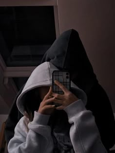 a person wearing a hoodie taking a selfie with their cell phone in front of them