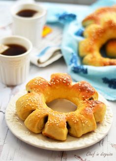 buns with sesame seeds on a plate next to two cups of coffee