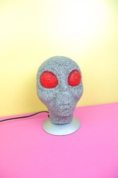 a gray skull lamp with red eyes on a pink surface