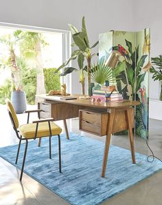 a desk with two chairs and a rug in front of it, surrounded by plants