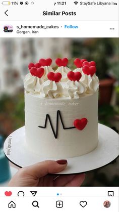 someone is holding up a cake with white frosting and red heart decorations on it