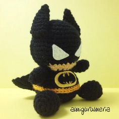 a crocheted batman stuffed animal sitting on top of a white table next to a yellow wall