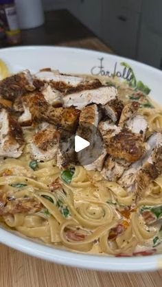 a white bowl filled with pasta and meat on top of a wooden table next to lemon wedges