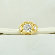 a yellow gold ring with three diamonds on it's side, sitting on a white cloth