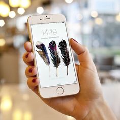 a woman is holding an iphone with feathers on the screen and she has red nails