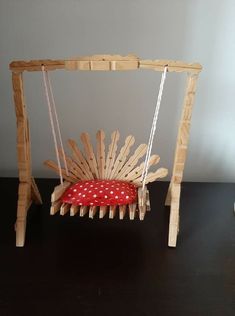 a toy swing made out of popsicle sticks with a red cushion on the seat