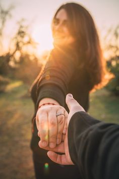 two people holding hands with the sun setting in the back ground behind them and trees