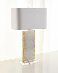 a marble lamp on a white table with a gray shade over the base and a gold trim around it