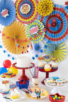 a table topped with cupcakes and cake next to paper fan decorating on the wall