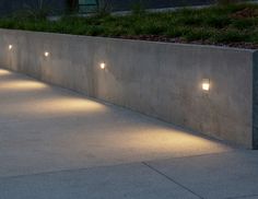 some lights that are on the side of a concrete wall and in front of grass