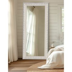 a large white framed mirror sitting on top of a wooden floor next to a bed