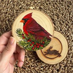 a hand holding a wooden ornament with a red bird on it