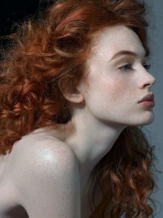 a red haired woman with freckles on her face and shoulders looking to the side