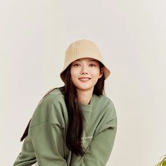 a young woman sitting on top of a wooden chair wearing a green sweater and hat