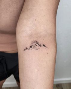 a woman's arm with a tattoo on it that has mountains in the background