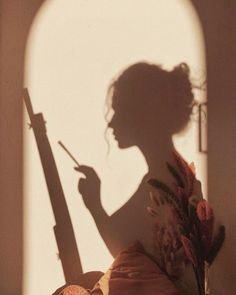 the shadow of a woman holding a paintbrush in front of a wall with an arched window