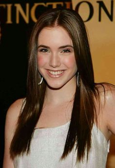 a woman with long brown hair smiling at the camera and wearing large hoop earrings on her head