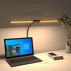 an open laptop computer sitting on top of a white desk next to a plant and book