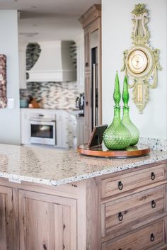 a green vase sitting on top of a counter next to a clock and oven in a kitchen