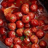 the meatballs are being cooked in the crockpot with sauce and parsley