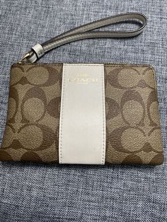 This Coach Corner Zip Wristlet in Signature Canvas is a fashionable accessory for any woman. The wristlet features a zip closure and wrist strap handle in a stylish beige color. The exterior is made of durable canvas material in a silver, khaki, and petal color scheme, with beige hardware accents. The wristlet includes a roomy interior lined with comfortable canvas and a convenient accessory pocket. The Coach logo is showcased on the front, and it comes with a wristlet accessory to complement its design. This wristlet is perfect for carrying your essentials and staying stylish on the go. Luxury Wristlet, Coach Logo, Signature Canvas, Wrist Strap, Beige Color, Canvas Material, Color Scheme, Bags Handbags, The Go