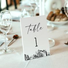 a table number is placed on top of a white table cloth with wine glasses and plates in the background