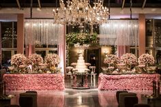 a wedding cake is displayed on a table with flowers and chandelier hanging from the ceiling