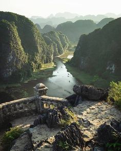 a river running through a valley surrounded by mountains and rocks in the foreground is a stone bridge with a tower on top