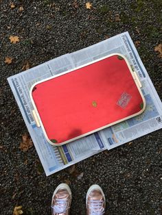 a person standing next to a red tray on top of a newspaper with their feet propped up