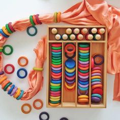 an assortment of colorful wooden beads and rings in a box with orange scarf around it