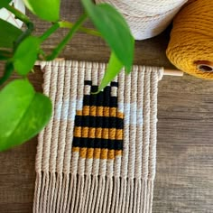 a woven wall hanging next to yarn and a potted plant on a wooden table