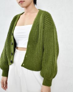 a woman wearing a green cardigan standing in front of a white wall