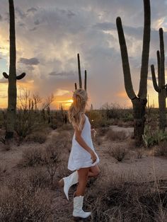 a woman in white dress walking through desert with cacti