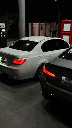 two cars parked next to each other in a parking lot with gas pumps on the side