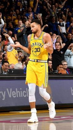 a basketball player is walking on the court with his arms in the air as fans look on