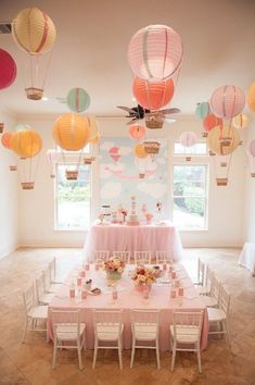 a table set up for a party with paper lanterns hanging from the ceiling above it