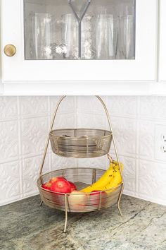 two metal baskets holding fruit on top of a counter