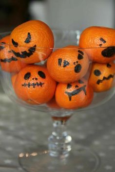 oranges with faces drawn on them in a glass bowl