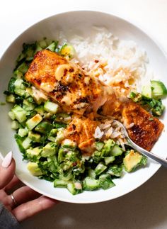 someone is holding a fork over a bowl of food with rice and cucumbers