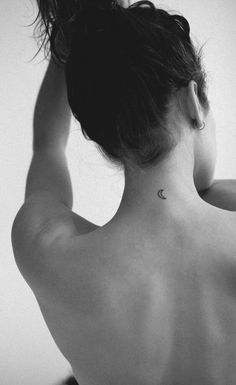 the back of a woman's neck with a small crescent tattoo on her left side