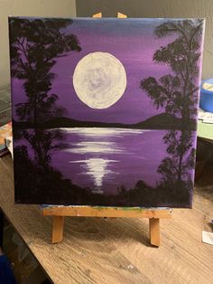 an easel with a painting on it that has a full moon in the sky